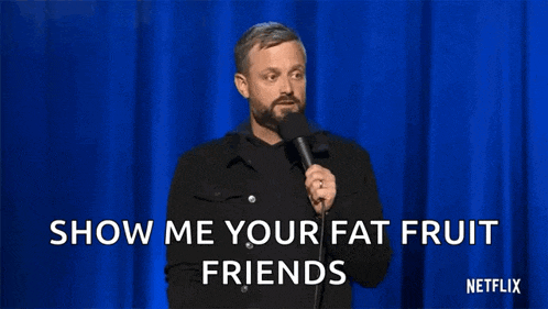 a man with a beard is holding a microphone on a stage and says show me your fat fruit friends .