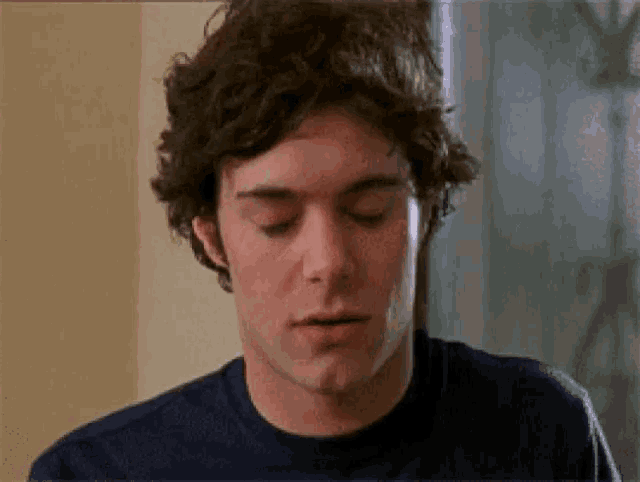 a man with curly hair is wearing a blue shirt and making a face .