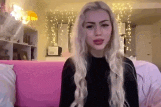 a woman with long blonde hair is sitting on a pink couch in a living room .