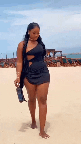 a woman in a black dress is walking on the beach with a bottle of wine .