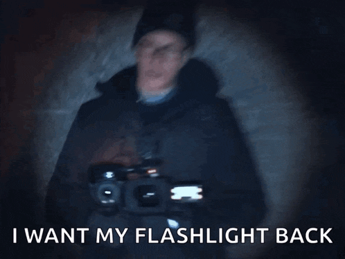 a man with glasses and a beanie is holding a flashlight and says " i want my flashlight back "