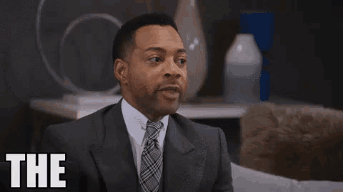 a man in a suit and tie is sitting in a living room and says `` the pressure is on '' .