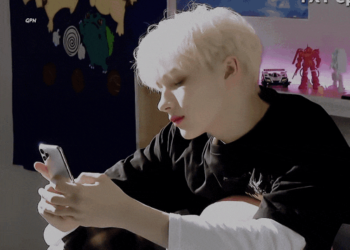 a boy with white hair is looking at his cell phone with a gpn logo in the corner