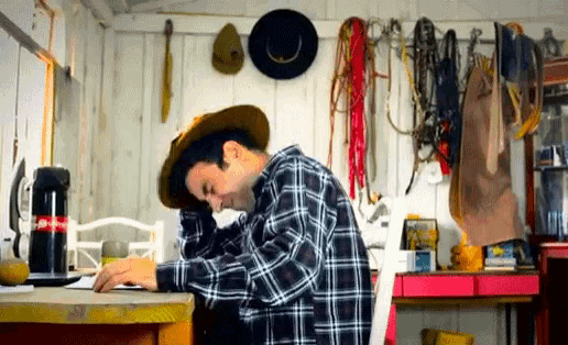 a man wearing a cowboy hat sits at a desk with a coca cola thermos on it