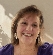a woman wearing a purple shirt is smiling for the camera