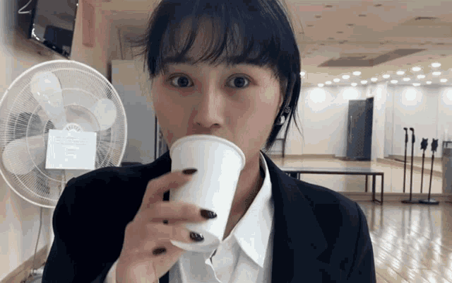 a woman drinking from a white cup in front of a fan that says ' n ' on it