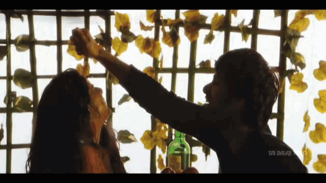 a man holds a bottle of wine and a woman reaches out to touch it