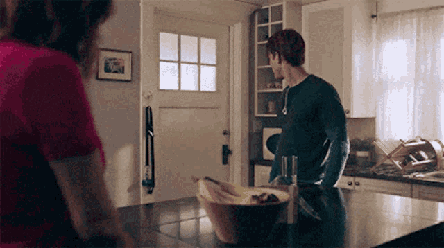 a man and a woman standing in a kitchen with a bowl of bananas