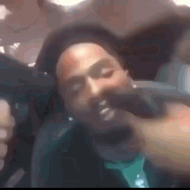 a man with a beard is sitting in a car with his eyes closed and a hand covering his mouth .
