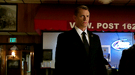 a man in a suit and tie stands in front of a red awning that says v. post 162