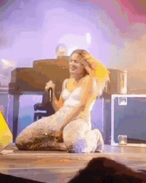 a woman in a white dress is kneeling down on a stage