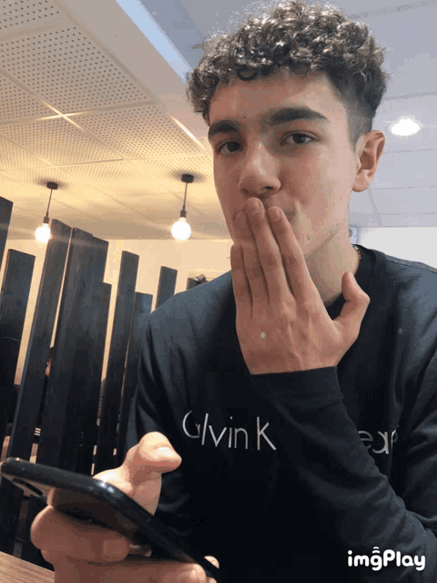 a young man wearing a black calvin klein sweatshirt holds a cell phone