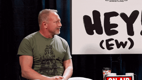 a man sits in front of a sign that says hey ew