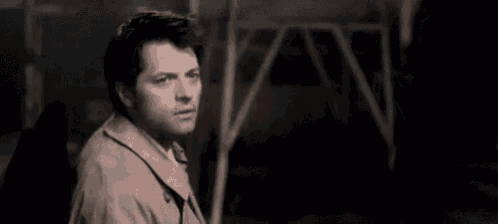 a man in a trench coat is standing in a dark room looking at something .