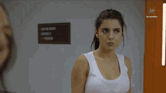 a woman in a white tank top is standing in front of a sign that says los estrellas