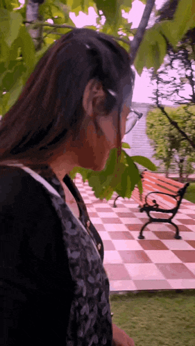 a woman wearing glasses stands in front of a bench