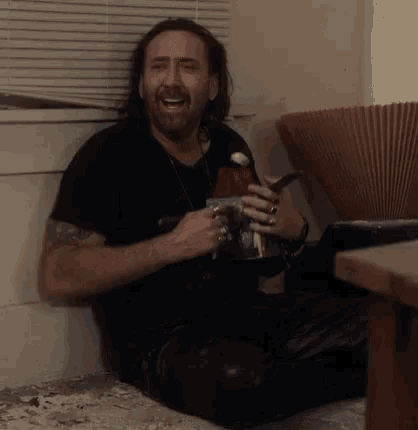 a man in a black shirt is sitting on the floor holding a cup