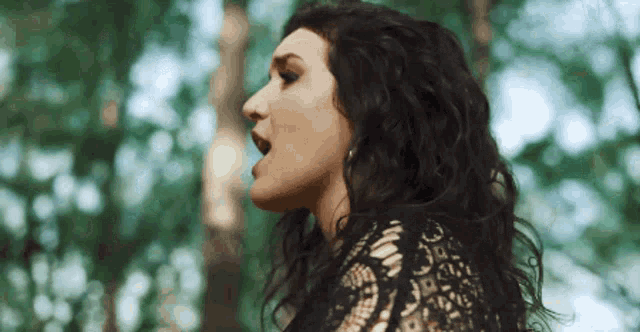 a woman with dark hair is singing in the woods .