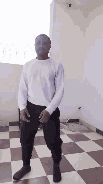 a man in a white shirt and black pants stands in front of a checkered floor