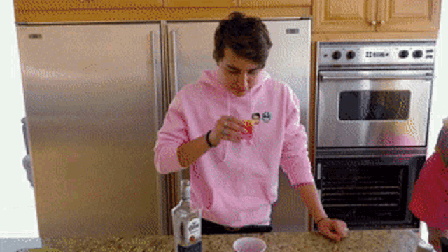 a man in a pink hoodie pours a drink into a cup