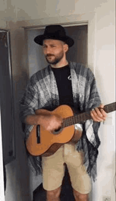 a man wearing a hat and a poncho is playing a guitar in a room .