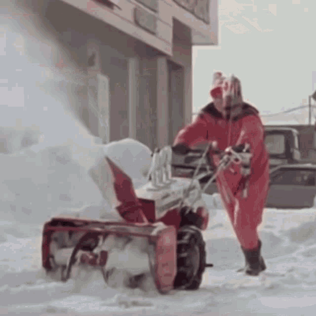 a man in a red suit is using a snow blower to clear snow