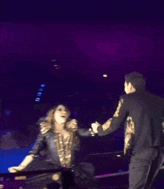 a man and a woman are dancing on a stage with purple lights in the background