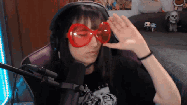 a girl wearing headphones and red glasses waves her hand in front of a microphone