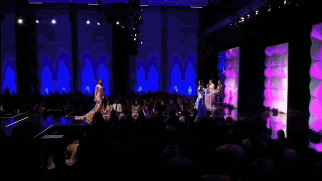 a woman in a purple dress is walking down a runway at a fashion show