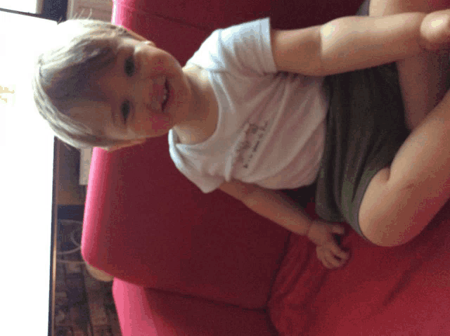 a little boy is sitting on a red couch wearing a white shirt that says i love you
