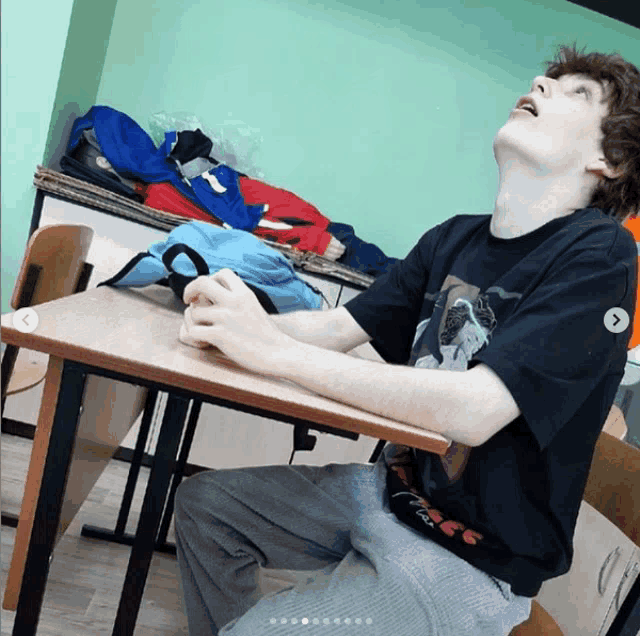 a man sitting at a desk with his eyes closed wearing a black shirt that says ' a ' on it