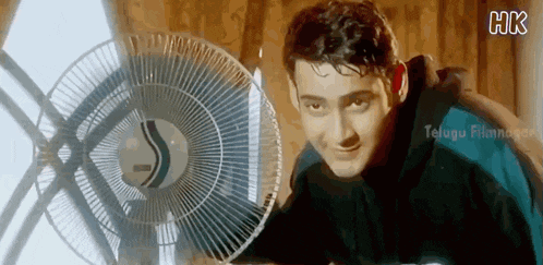 a man is standing next to a fan in a room and smiling .