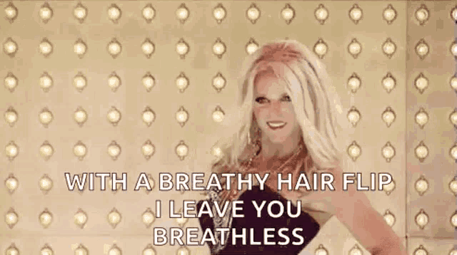 a woman in a black dress is standing in front of a wall with lights on it and a breathy hair flip .