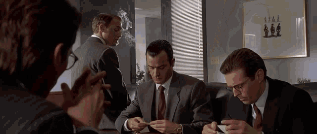 a group of men in suits and ties are sitting around a table smoking cigarettes and drinking coffee