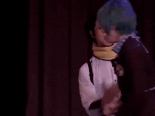 a man with blue hair is talking to another man with a scarf around his neck