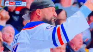 a man with a beard is wearing a hat and a hockey jersey while watching a game .