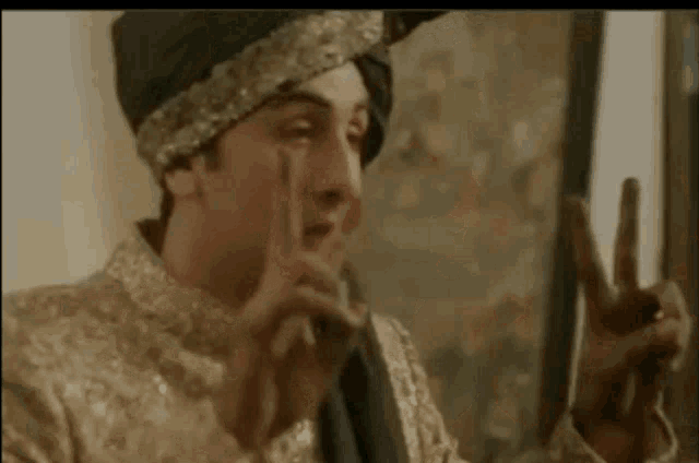 a man wearing a turban and a gold dress is making a peace sign with his hands .