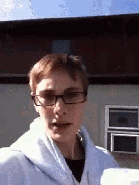 a young man wearing glasses and a white sweatshirt stands in front of a building