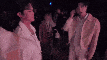 two men are standing next to each other in a dark room talking on a cell phone .