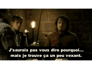 a man in a red shirt is talking to another man in a dark room in french