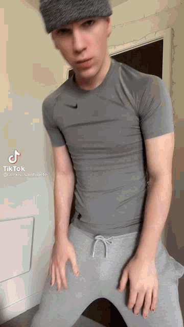 a young man wearing a gray shirt and gray sweatpants is standing in a room .