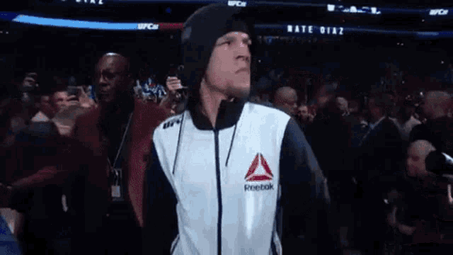 a man in a reebok jacket is walking through a crowd of people in a boxing ring .