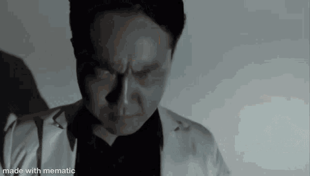 a man in a white suit and black shirt is looking down in a black and white photo made with mematic .
