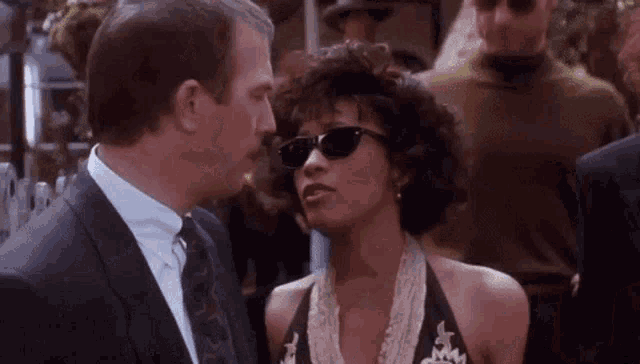 a man and a woman wearing sunglasses are standing next to each other and kissing .