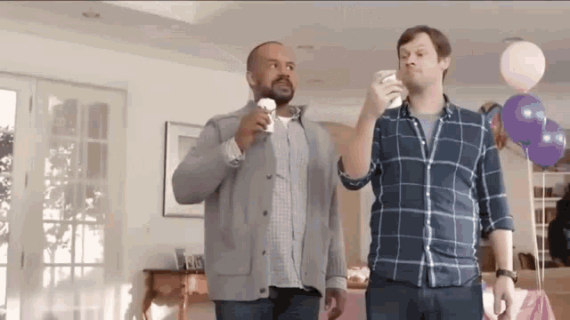 two men are standing next to each other in a room with balloons