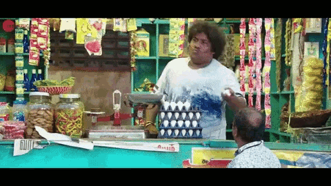 a man standing behind a counter in a store talking to another man with a stack of eggs on it
