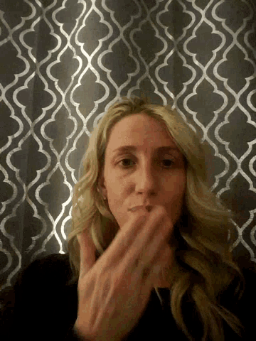 a woman covering her mouth with her hand in front of a wall with a geometric pattern