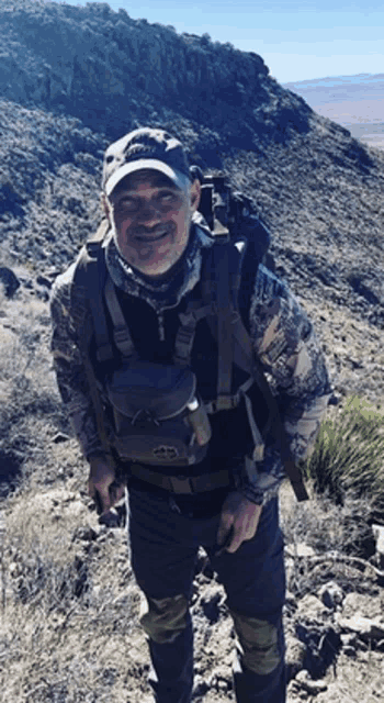 a man standing on top of a hill with a backpack and a hat that says ' jackson ' on it