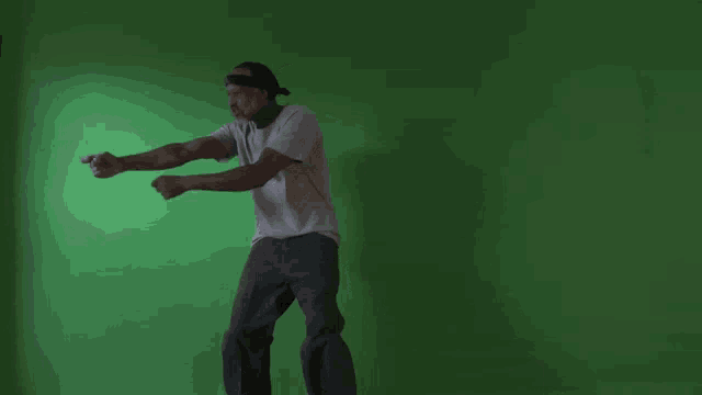 a man in a white shirt and gray pants stands in front of a green screen