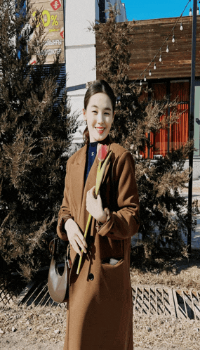 a woman in a brown coat is holding a flower